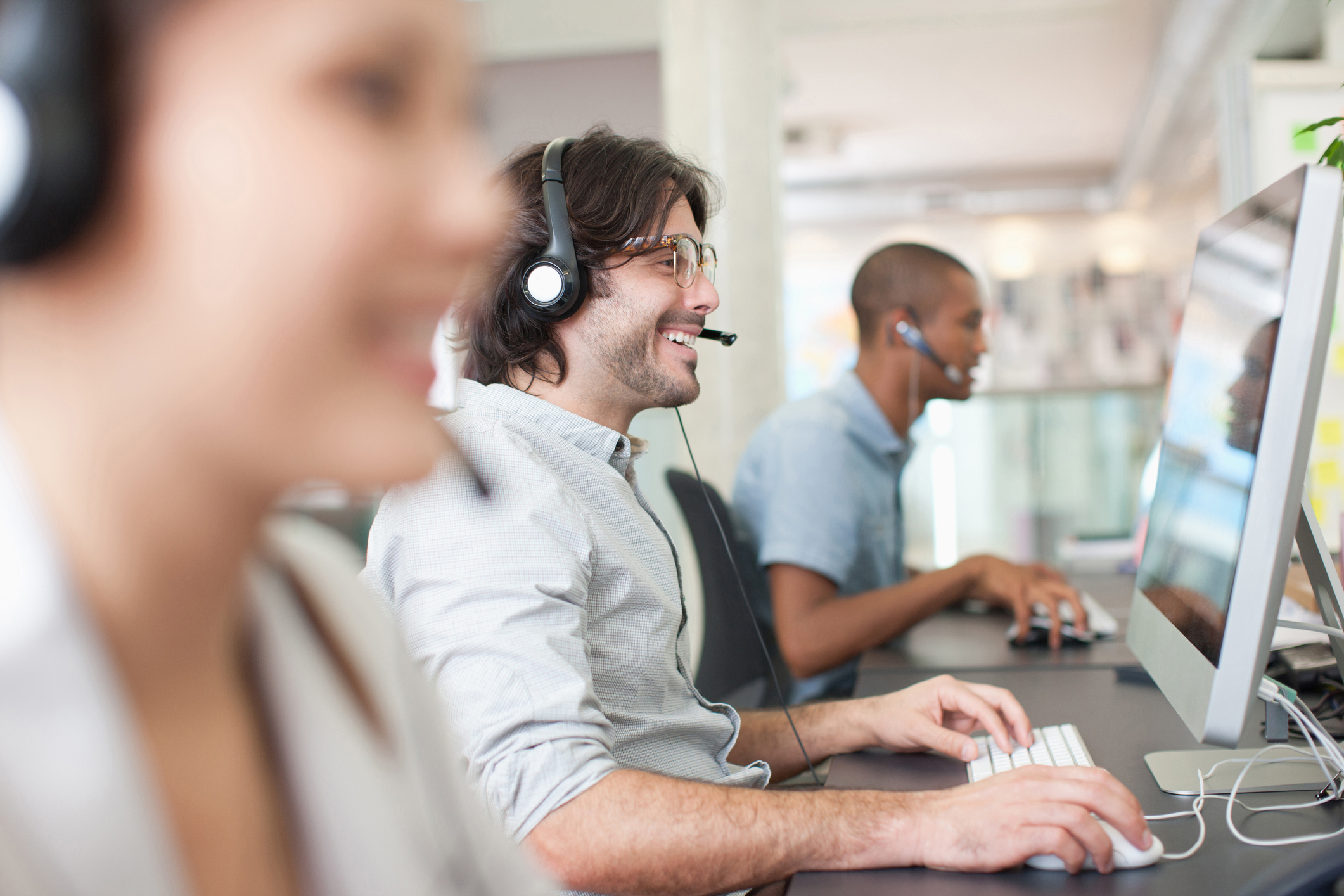 Man working next to coworkers, on a headset smiling.